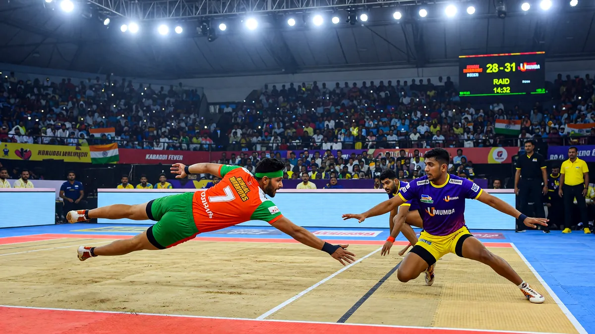 A raider and corner defender in mid-tackle during a Pro Kabaddi evening match